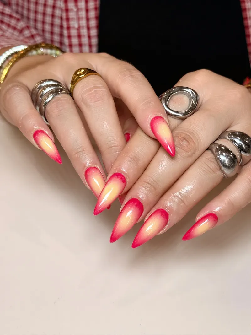 Ongles stiletto en dégradé rouge corail et jaune pâle, bagues argent et or